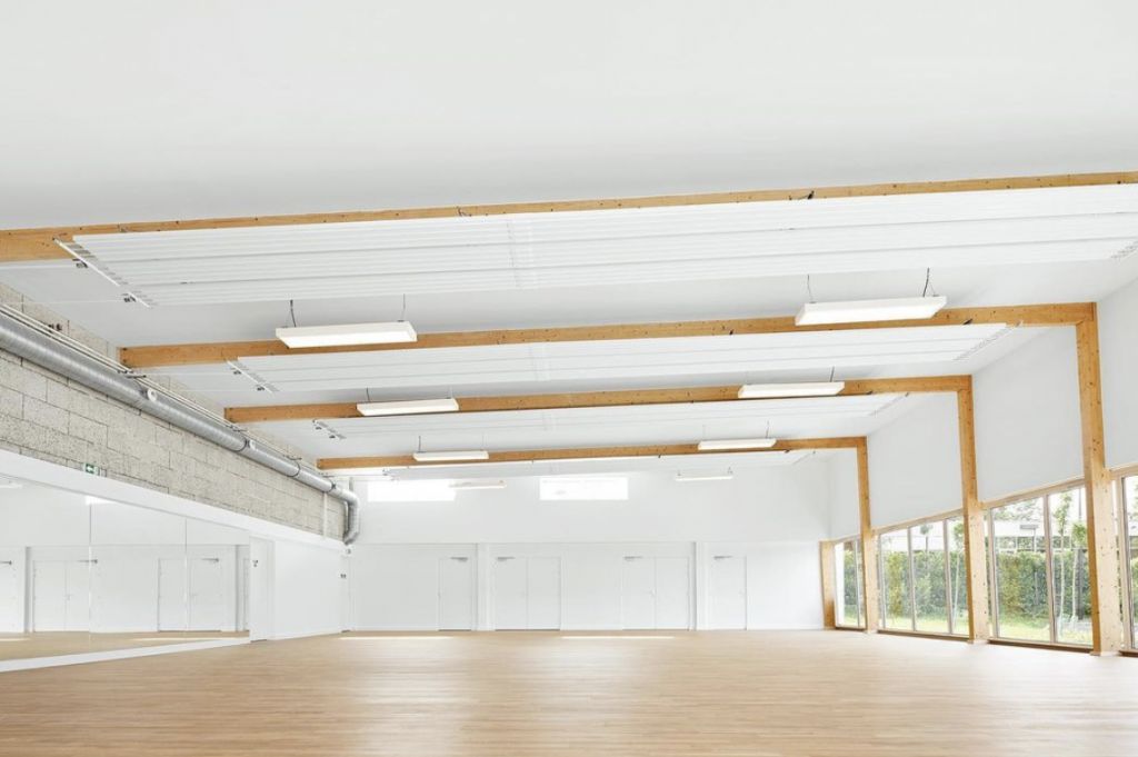 Hempcrete: The interior of a white sports hall with blonde wood floors and light from the windows on the right side 