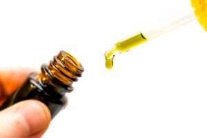 A brown bottle of CBD with a dropper held above it dripping yellow oil 