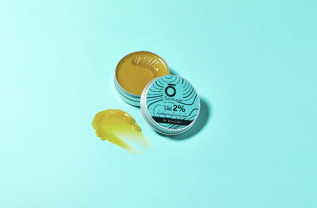 The good level: CBD balm on a blue background with a smudge of balm beside the open tin