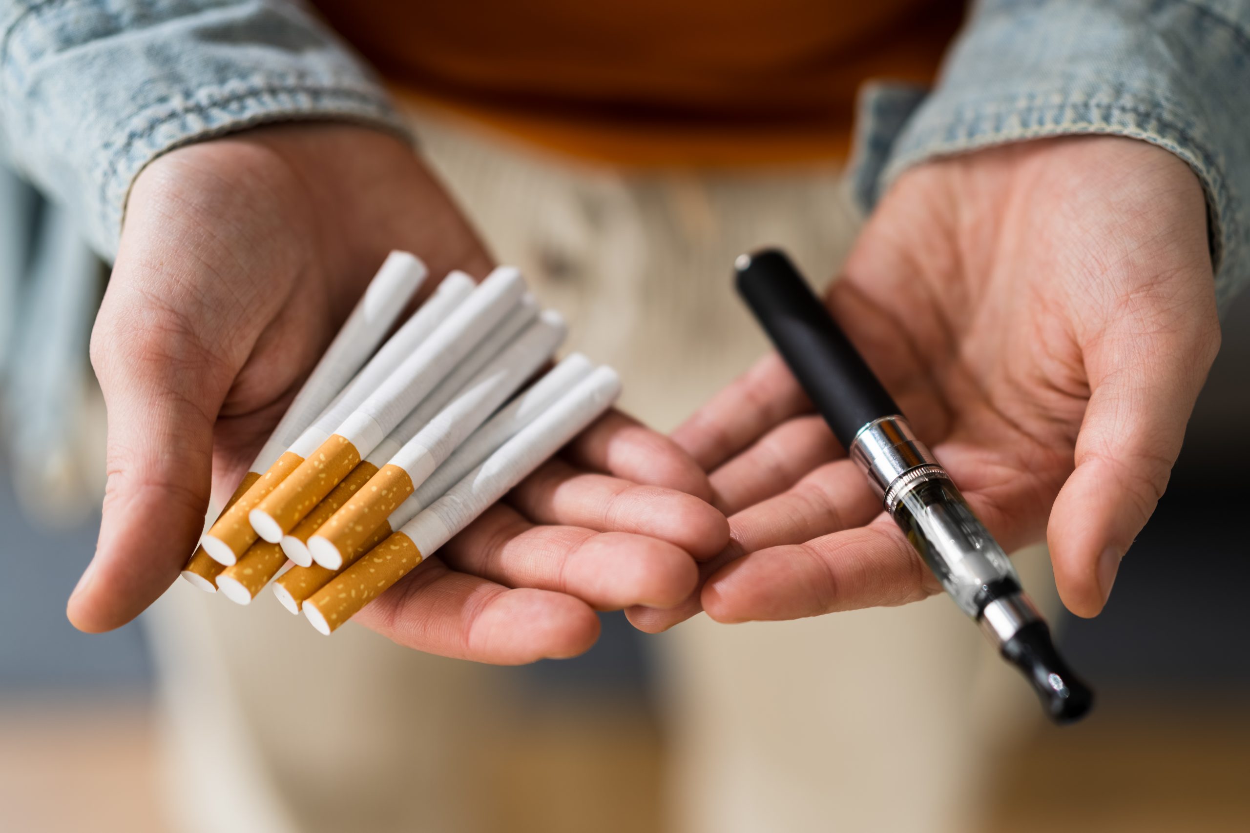 Smoking: A hand holding out cigarettes and another with a CBD vape